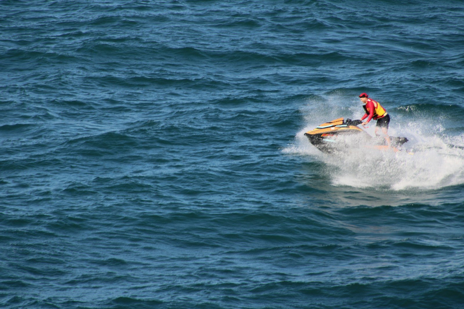 Un pilote lancé sur un jet-ski, gerbe d'eau derrière la machine